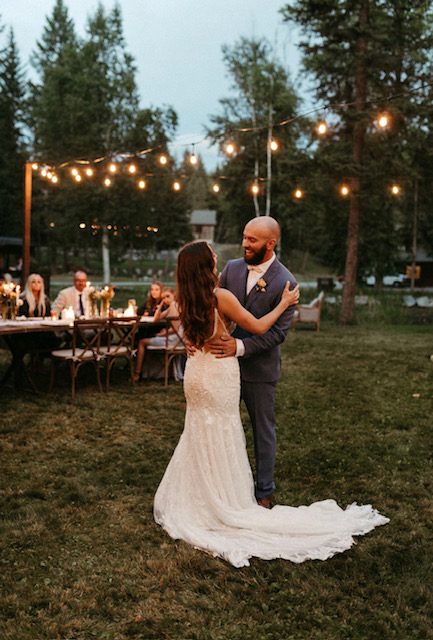 A couple's first dance on the lawn at dusk, string lights overhead