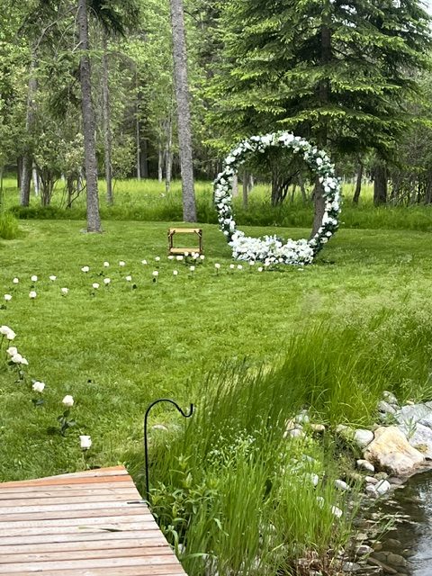 Green grass and wildflowers along the pond, with a flower arch beyond